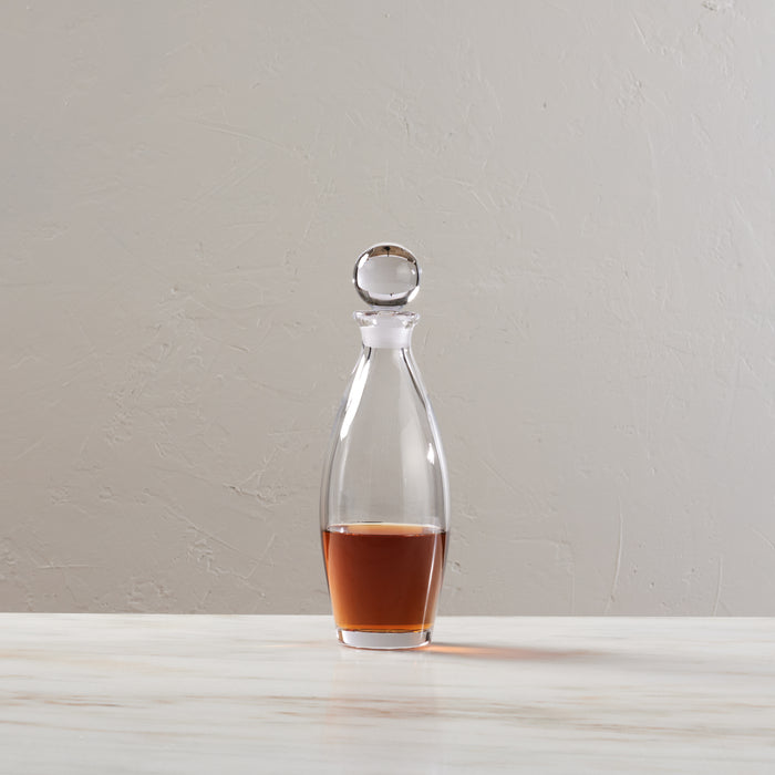 Clear glass decanter with spherical stopper, partially filled with amber liquid.
