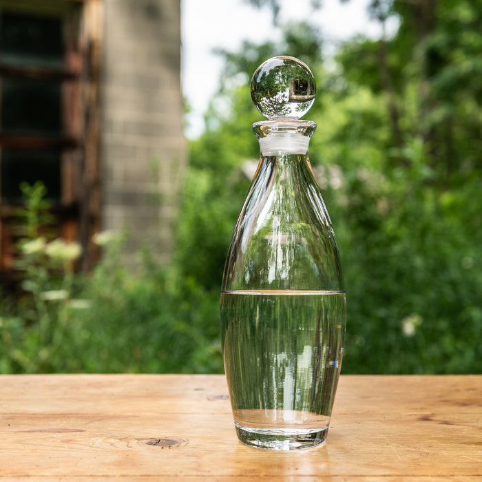 Clear glass decanter with spherical stopper, textured body, and horizontal band detail, displayed on wooden surface.