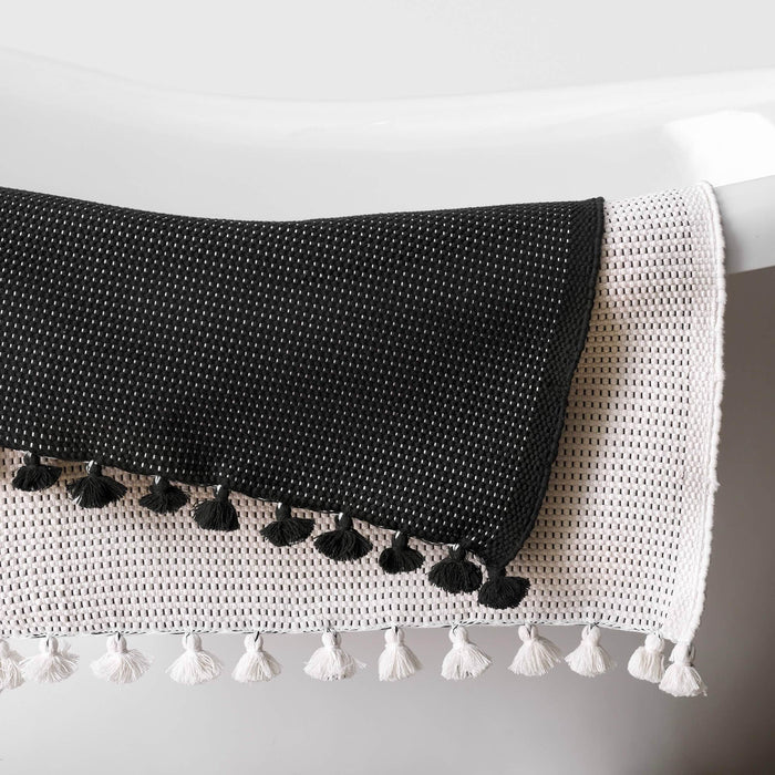 Cream bath mat with tassels overlaid with black bath mat with tassels
