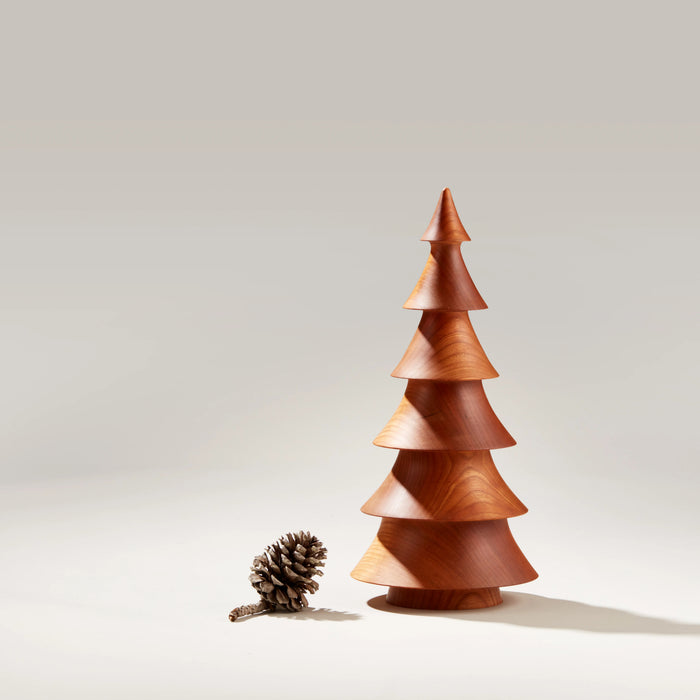 Wooden evergreen tree sculpture in cherry wood with tiered conical sections and a pinecone beside it.