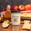 Serendipity "Apple Maple Bake" candle with apples, pie, and cookies on a wooden table