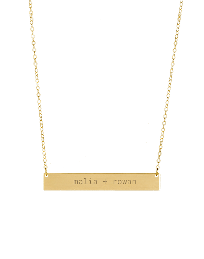 Gold bar necklace engraved with custom text on plain background