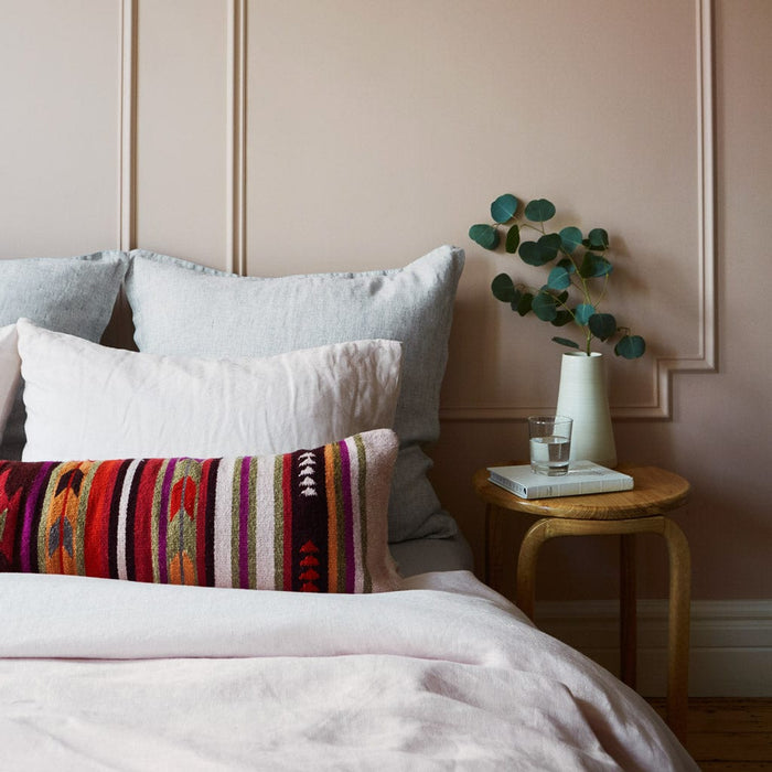 Geometric and striped oversized lumbar pillow styled on bed with side table, multicolor