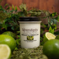 Serendipity Soy Candle Company Candle with 'Bergamot, Cypress & Lime" label surrounded by greenery and limes