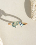 Gold band ring featuring a pear-shaped green stone and square blue topaz stone in silver prong settings