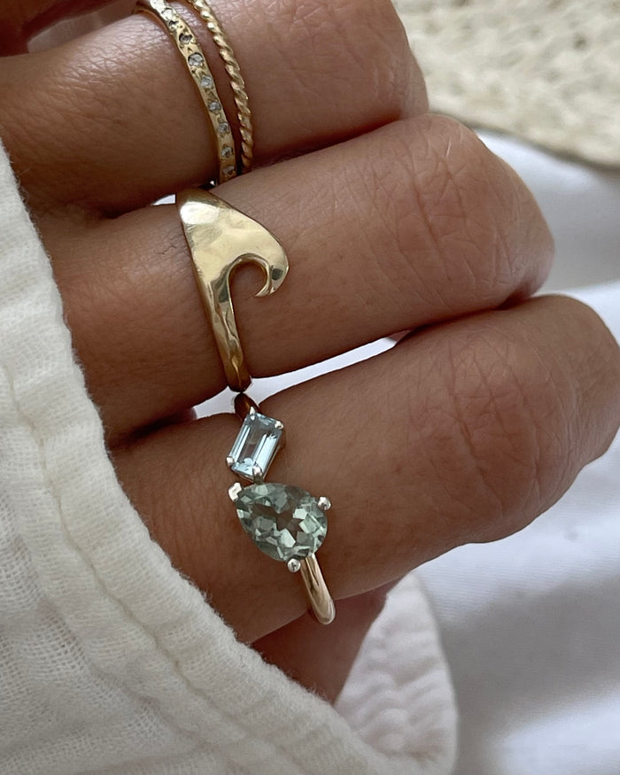 Gold band ring featuring a pear-shaped green stone and square blue topaz stone in silver prong settings