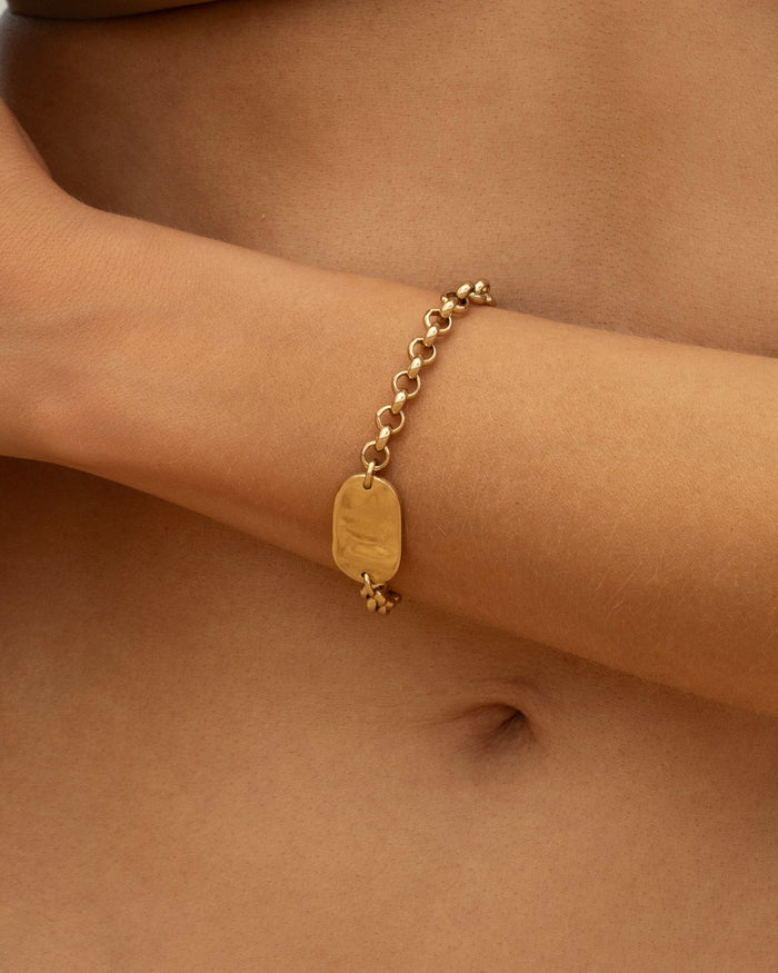 Gold chunky rolo chain bracelet with rectangular polished ID plate, lifestyle shot worn by model