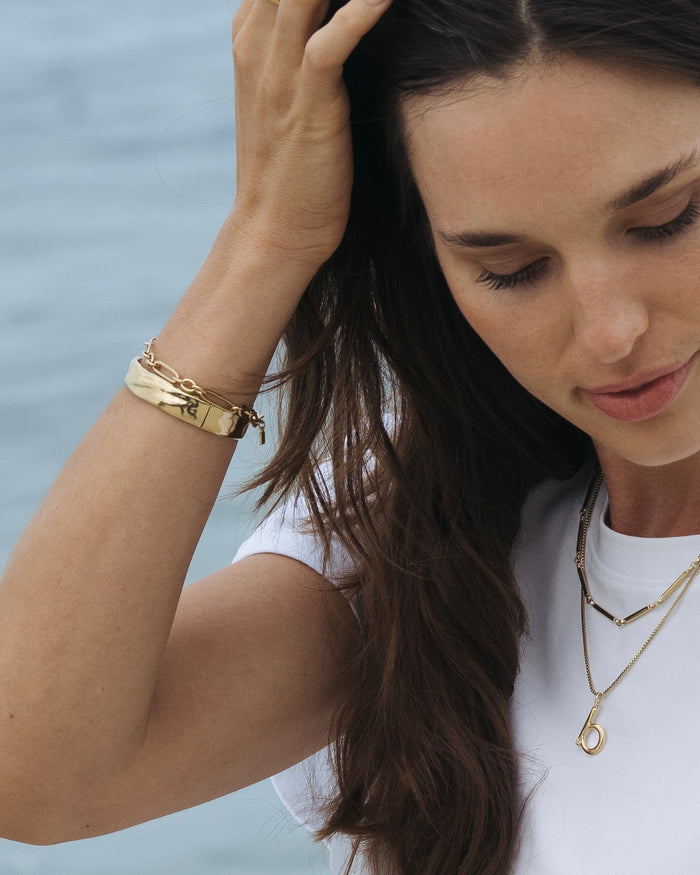 Woman at the beach wearing gold jewelry, touching her hair
