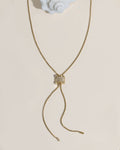 Gold box chain lariat necklace with a crystal-encrusted cylindrical slider bead and dangling chain ends on cream surface