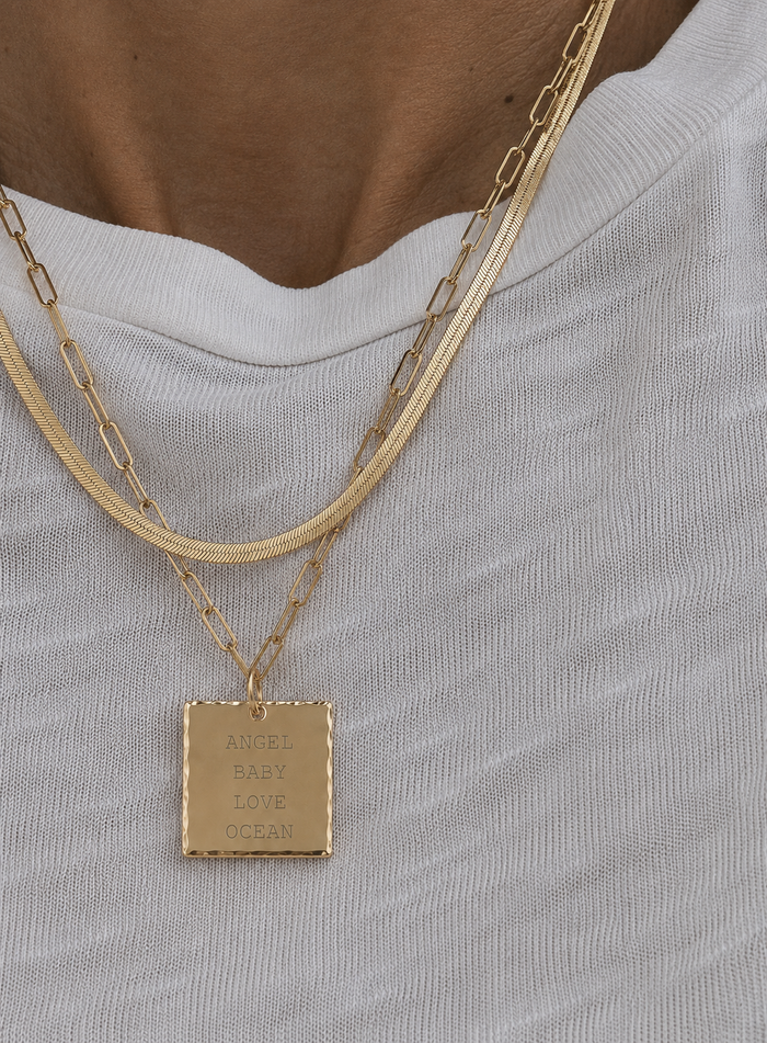 Model wearing layered necklaces with large engraved square pendant