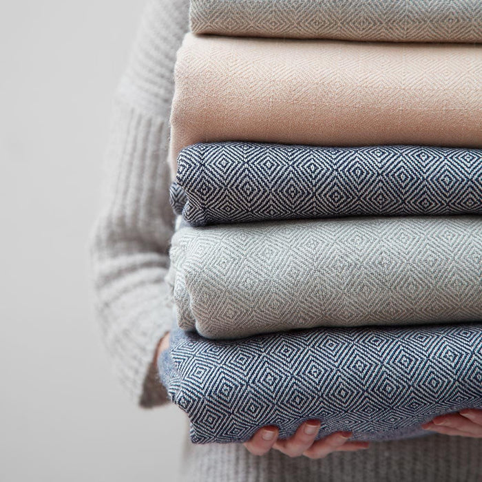 woman holding stack of alpaca throw blankets, dove-grey