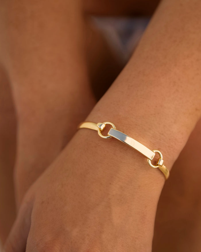 Model wearing gold bangle bracelet with bar and hardware clasp on wrist