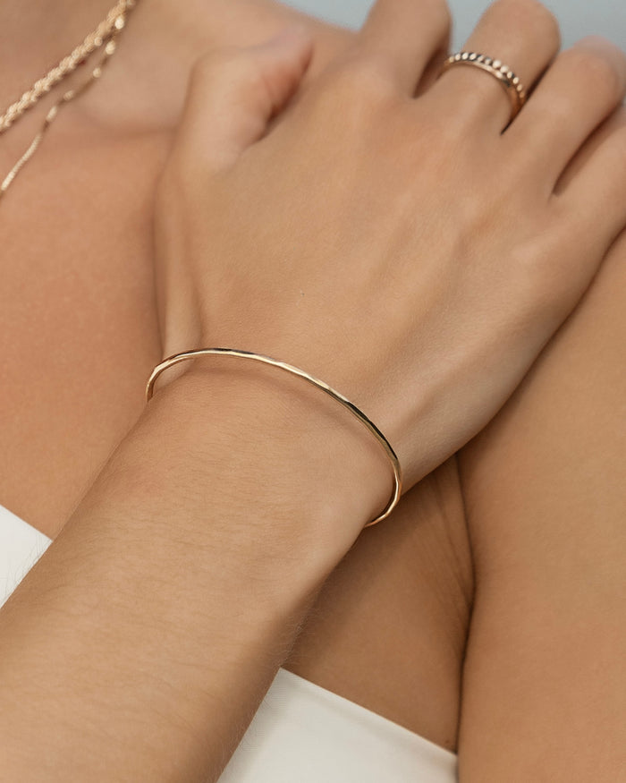 Model wearing thin gold open cuff bracelet on wrist