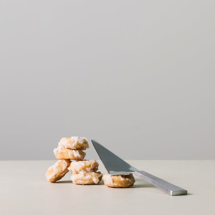 Silver pie and cake server with gray handle displayed next to stacked pastries on white surface.
