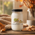 Candle jar with 'Hello Fall' label on a wooden surface with autumn leaves and decor.