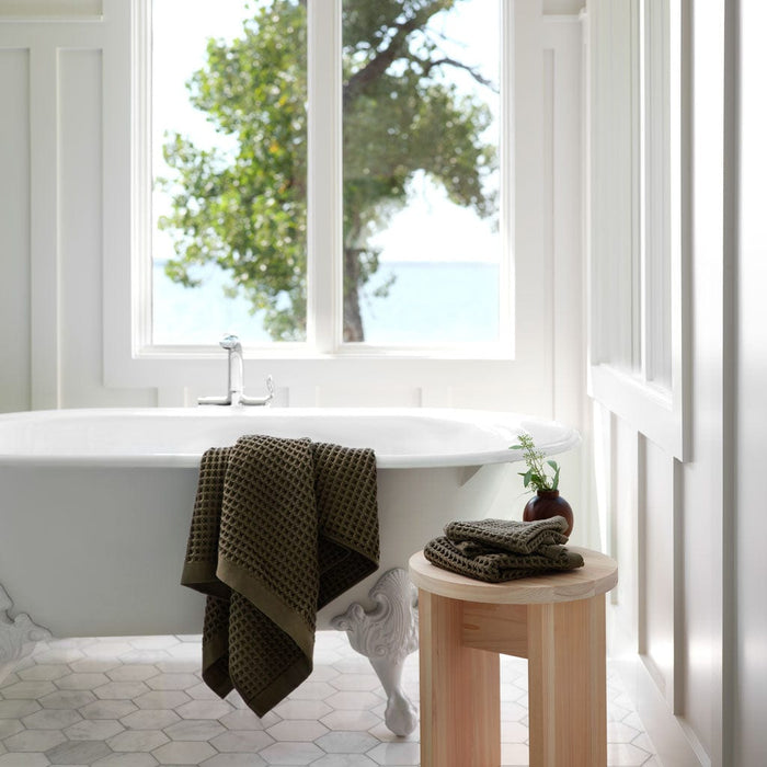 Green waffle towel draped over edge of bathtub, olive