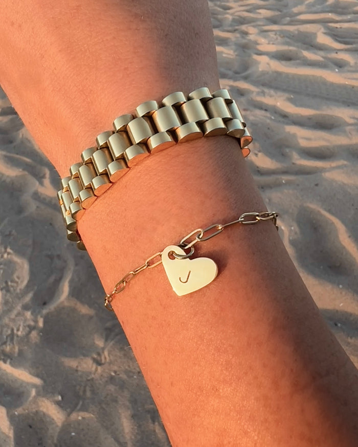 Model wearing layered gold bracelets with heart charm