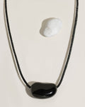 Black cord necklace with a polished black organic-shaped stone pendant on cream surface