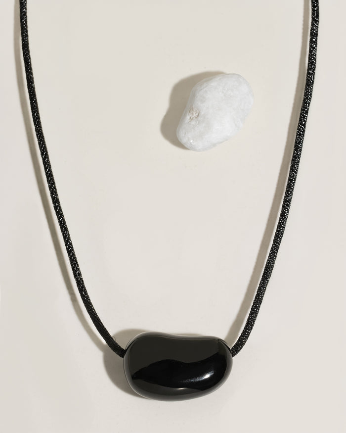 Black cord necklace with a polished black organic-shaped stone pendant on cream surface