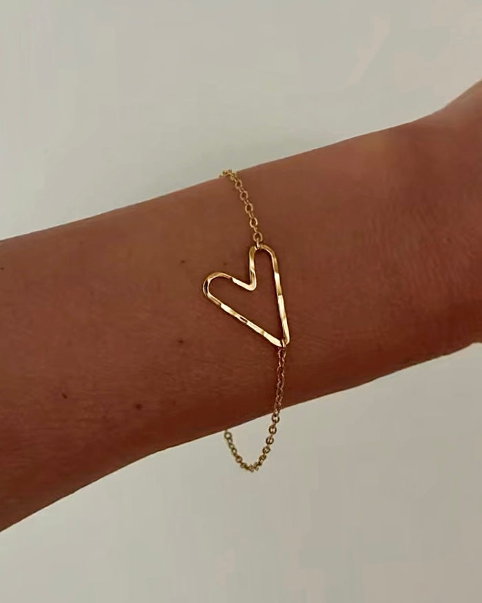 Model wearing gold chain bracelet with open-outline heart charm on wrist