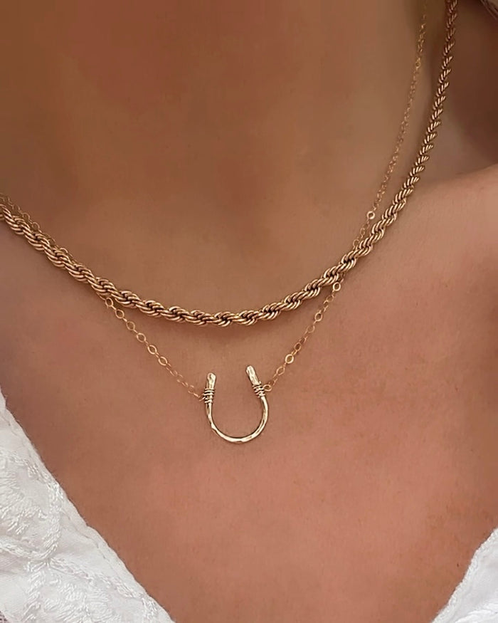 Model wearing layered gold horseshoe necklace with rope chain