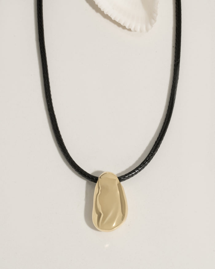 Gold necklace with a dark pendant worn on a model