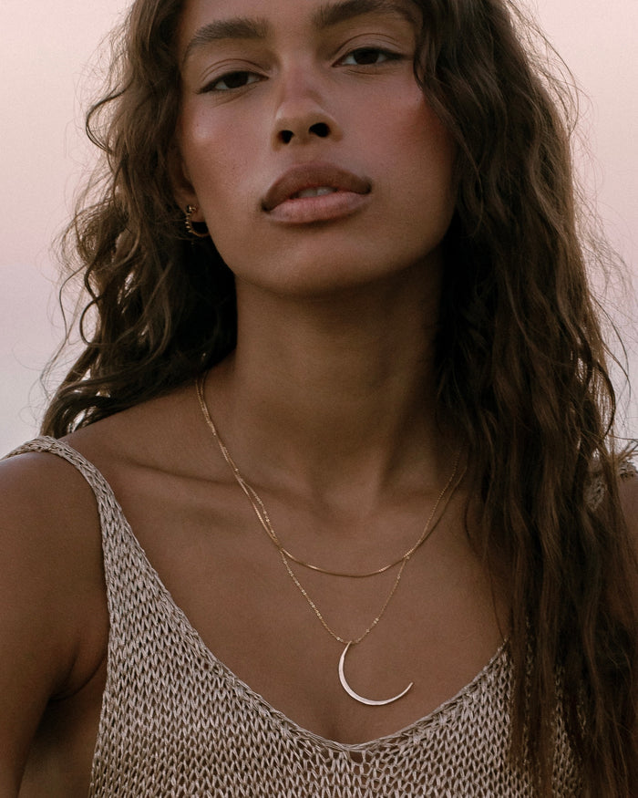 Model wearing layered gold necklaces with crescent moon pendant