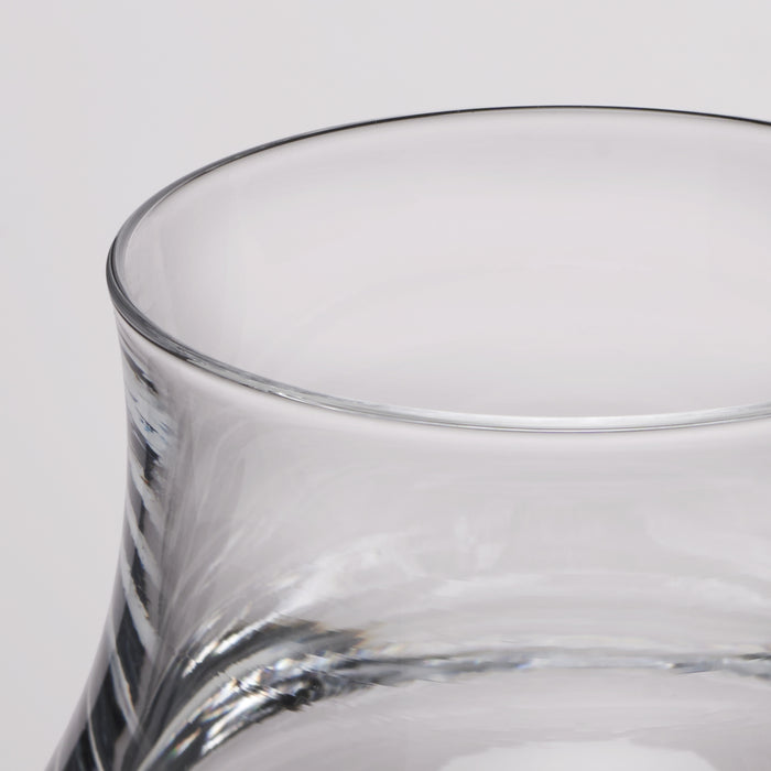 Close-up of a clear glass with a flared rim and subtle spiral texture on the lower body, photographed against a light gray background.