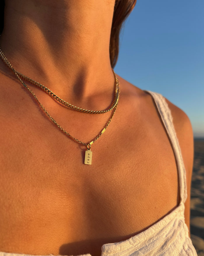Model wearing layered necklace with small engraved name charm
