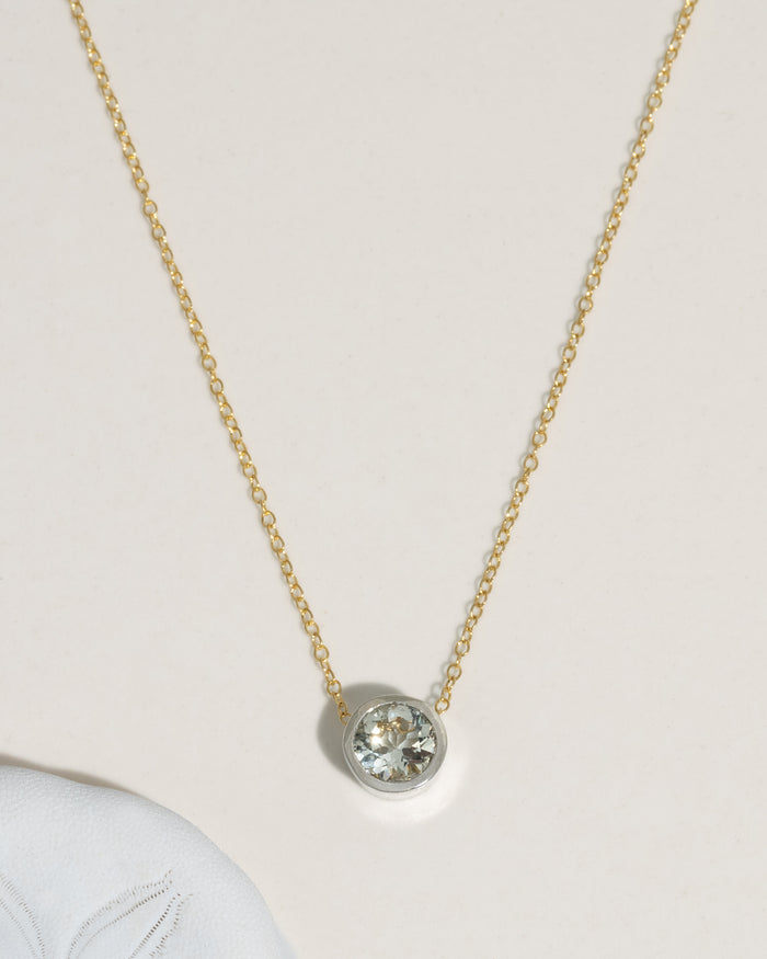 Delicate gold cable chain necklace with bezel-set round diamond solitaire pendant on cream background