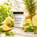 Candle labeled 'The Serendipity' with pineapples and cilantro on a natural background