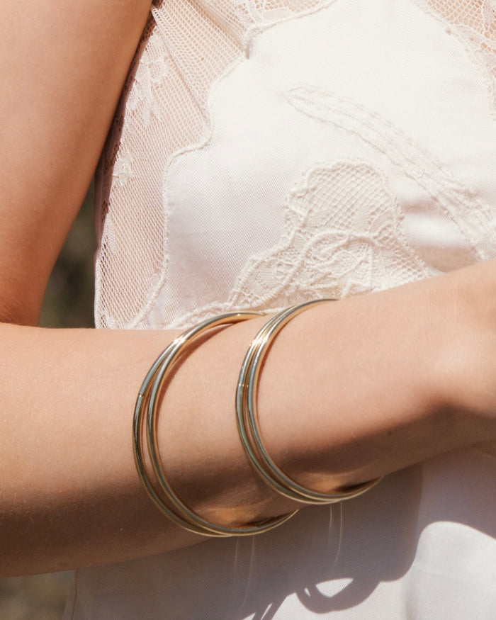Model wearing multiple thin gold bangle bracelets stacked on wrist