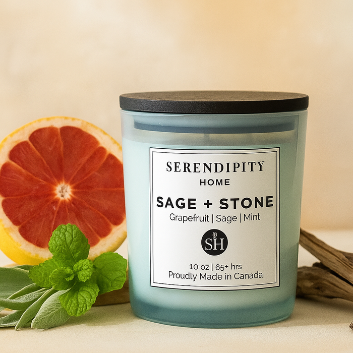 A Serendipity Home candle with 'Sage + Stone' label next to a slice of grapefruit. mint and sage leaves on a beige background