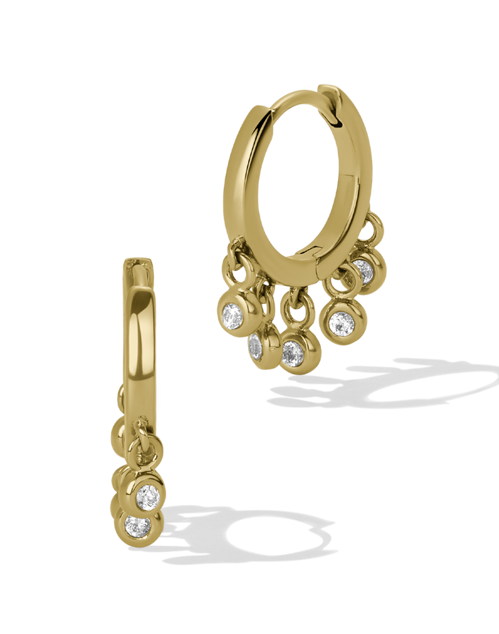 Gold huggie hoop earrings with bezel-set crystal drops along the lower half of the hoop