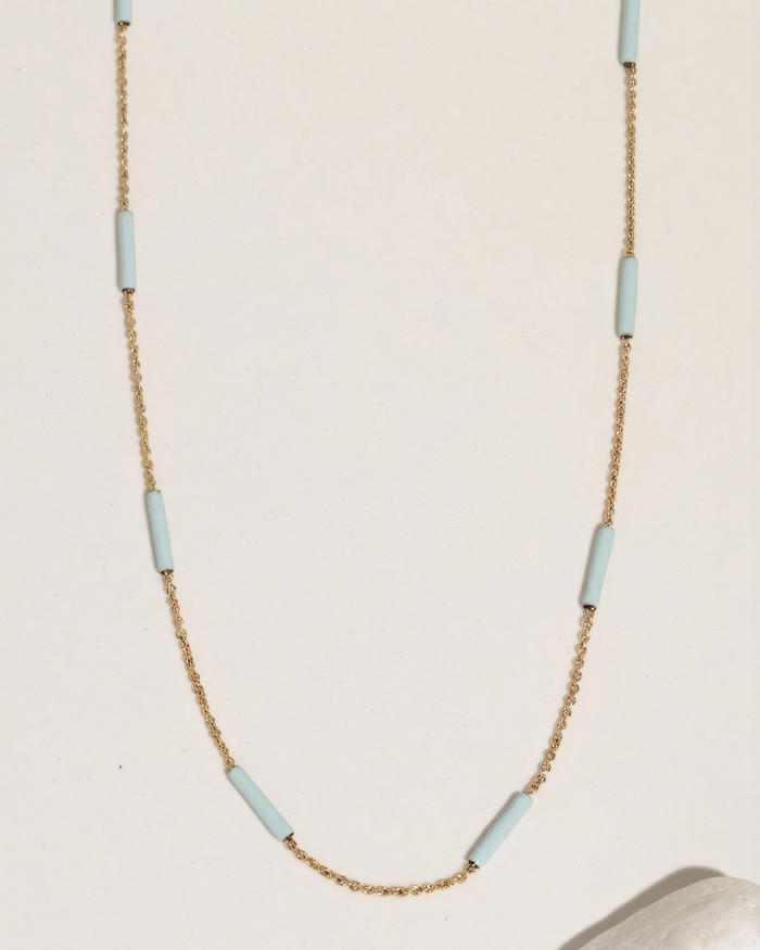 Gold chain necklace with a blue accent, flat lay