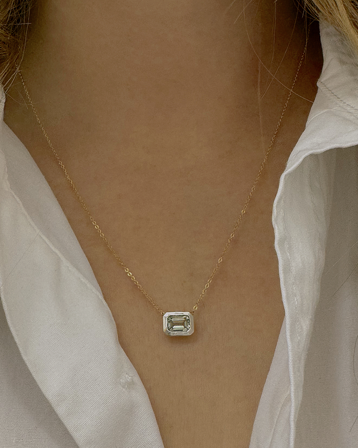 Model wearing a delicate gold chain necklace with a small emerald-cut gemstone in silver bezel pendant over a white shirt