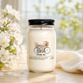 Jar candle labeled 'Spring Air' with a bicycle and flowers design, placed on a wooden surface with white flowers in the background.