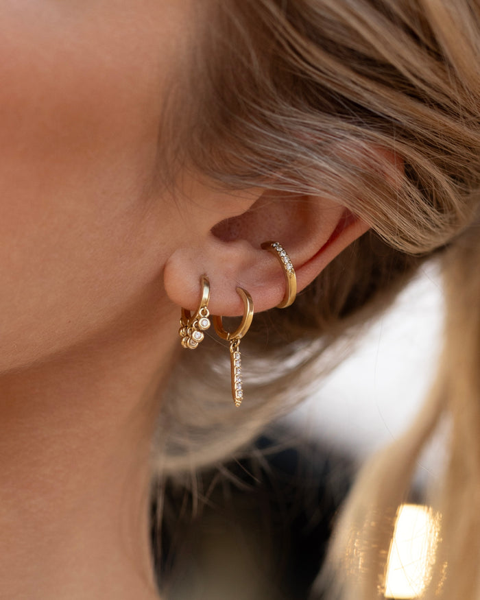 Gold huggie hoop earrings with bezel-set crystal drops along the lower half of the hoop, lifestyle shot worn by model