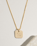 Gold tablet pendant necklace engraved with two initials, close-up