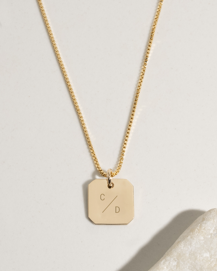 Gold tablet pendant necklace engraved with two initials, close-up