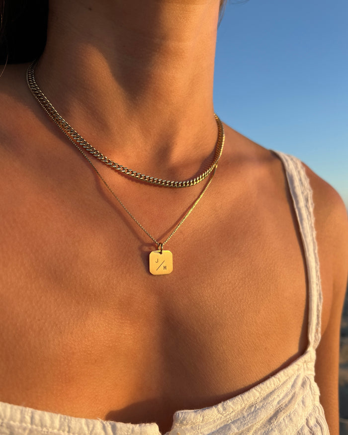 Model wearing layered tablet pendant necklace with curb chain