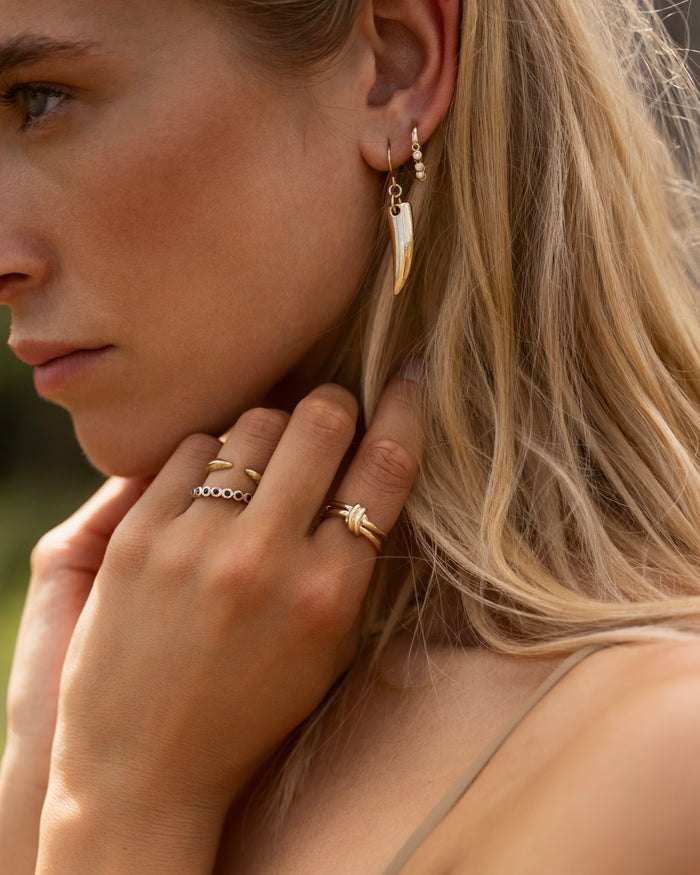 Gold drop earrings with polished talon or horn-shaped pendants on fish hook wires, lifestyle shot worn by model