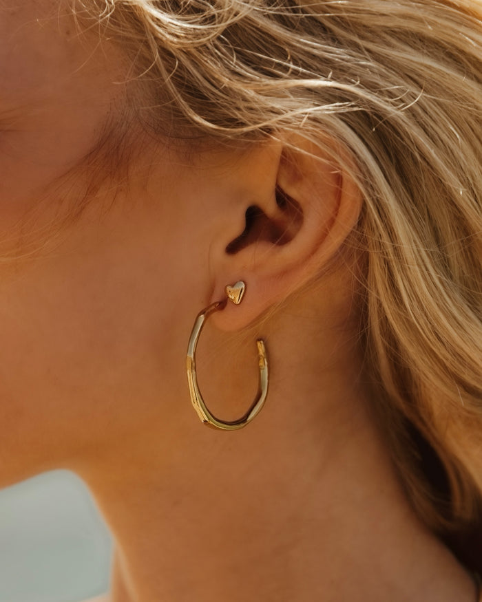 Small gold heart stud earrings worn on a model